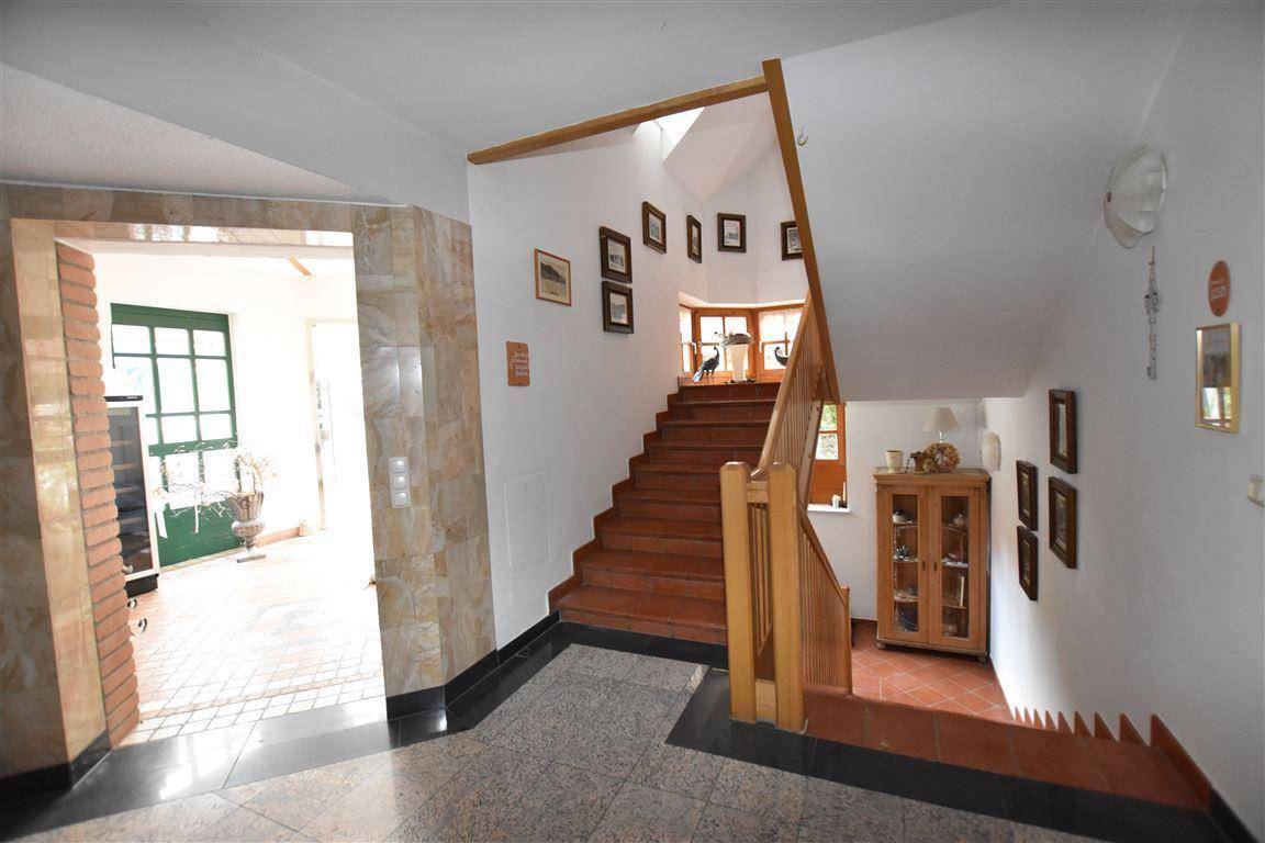 Eingangsbereich mit Holztreppe, gefliestem Boden und einem Fenster im Treppenhaus.