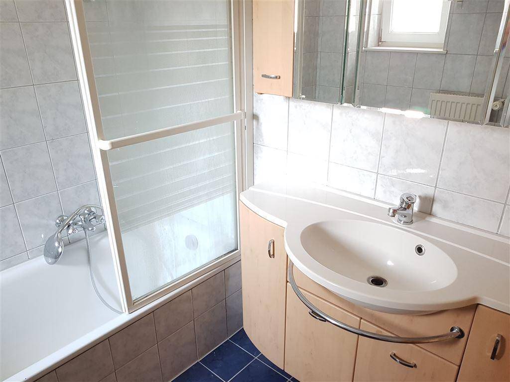 Badezimmer mit Badewanne, Duschabtrennung, Einzelwaschbecken und blauen Bodenfliesen.