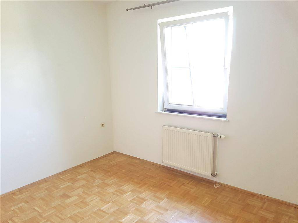 Helles Schlafzimmer mit Parkettboden, weiß gestrichenen Wänden und einem großen Fenster.