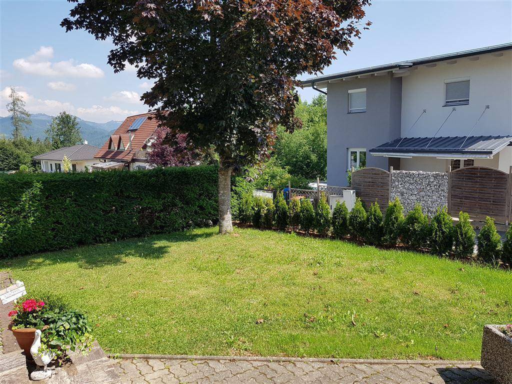 Gepflegter Gartenbereich mit Rasenfläche, Bäumen und Hecken, angrenzend an ein Nachbarhaus.