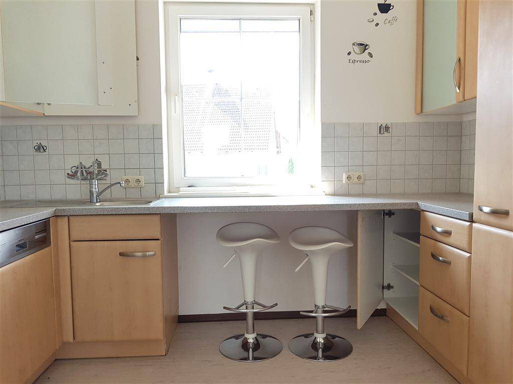 Funktionale Küche mit hellen Holzschränken, Fliesenrückwand und integrierter Frühstücksbar.
