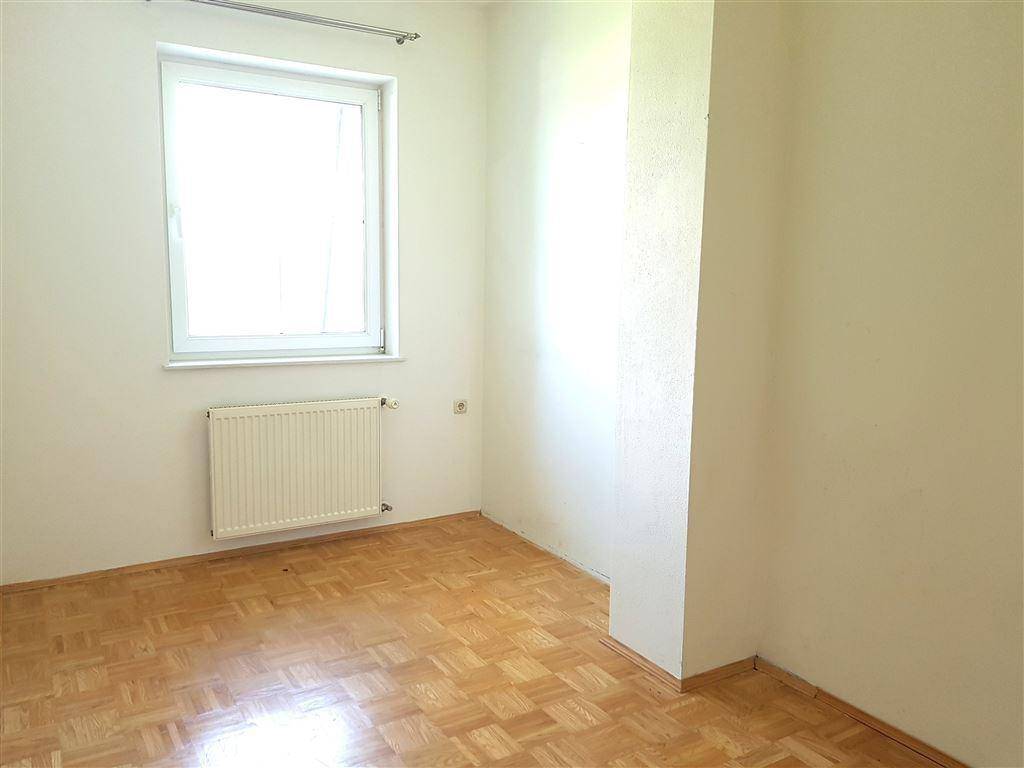 Leeres Schlafzimmer mit Parkettboden und einem Fenster, das viel Tageslicht hereinlässt.