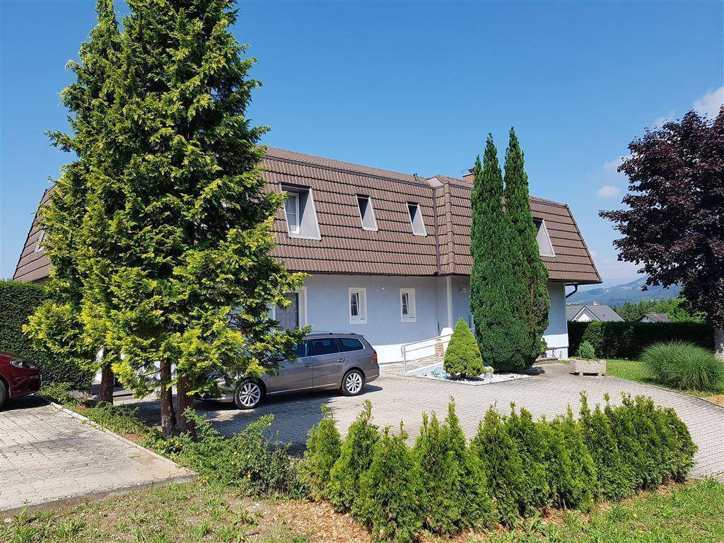 Außenansicht des Hauses mit Mansarddach, gepflasterter Einfahrt und gepflegter Bepflanzung.