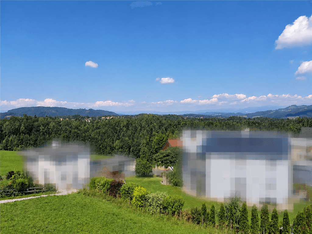 Weitläufiger Blick über grüne Hügel und Wälder mit vereinzelten Häusern in der Ferne.