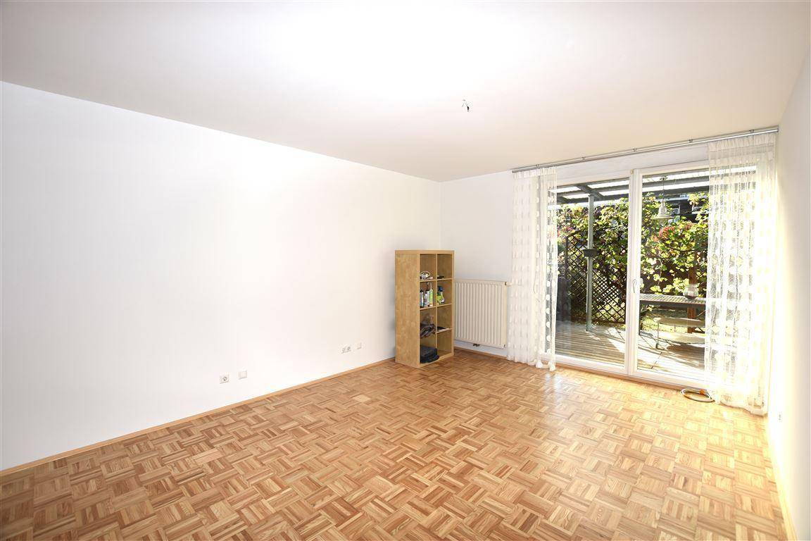 Geräumiges Wohnzimmer mit Parkettboden und großer Schiebetür zur überdachten Terrasse.