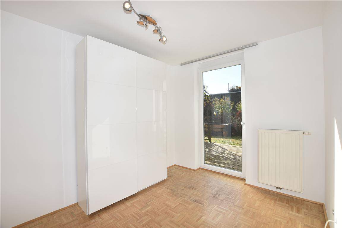 Helles Zimmer mit Parkettboden, weißem Kleiderschrank und Zugang zum Garten.
