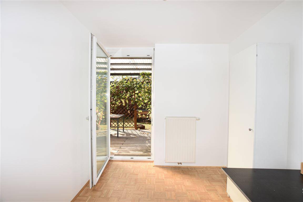 Heller Raum mit Parkettboden und großen Glastüren, die zu einer überdachten Terrasse führen.