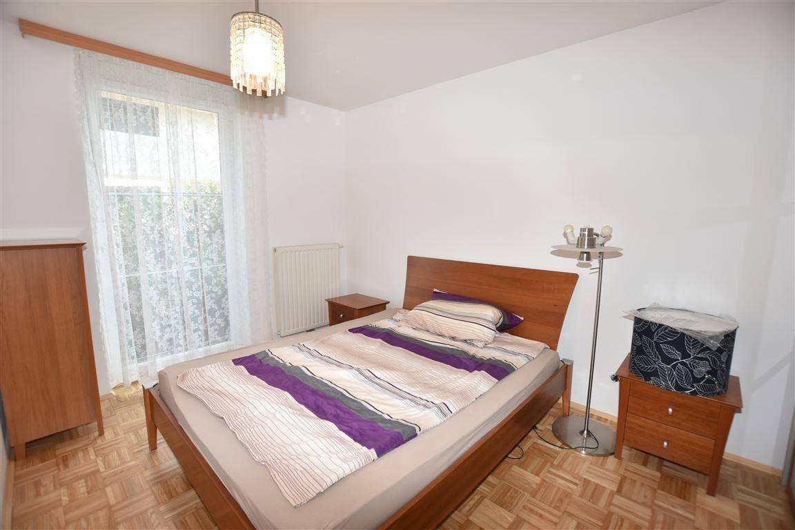Gemütliches Schlafzimmer mit Holzbett, Parkettboden und Fenster mit Blick ins Grüne.