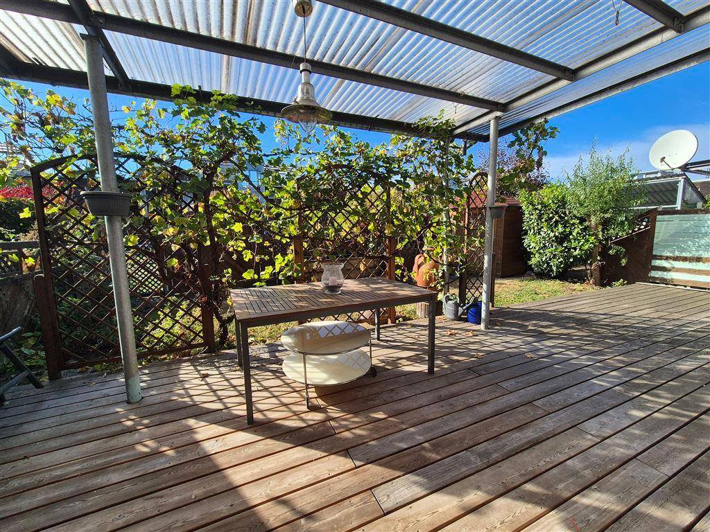 Überdachte Holzterrasse mit Esstisch und üppiger Begrünung im Garten.