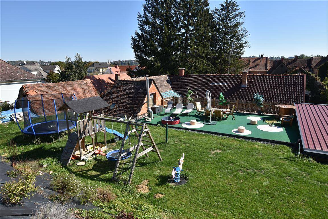 Großer Garten mit Spielplatz, Trampolin und einer sonnigen Terrasse im Hintergrund.