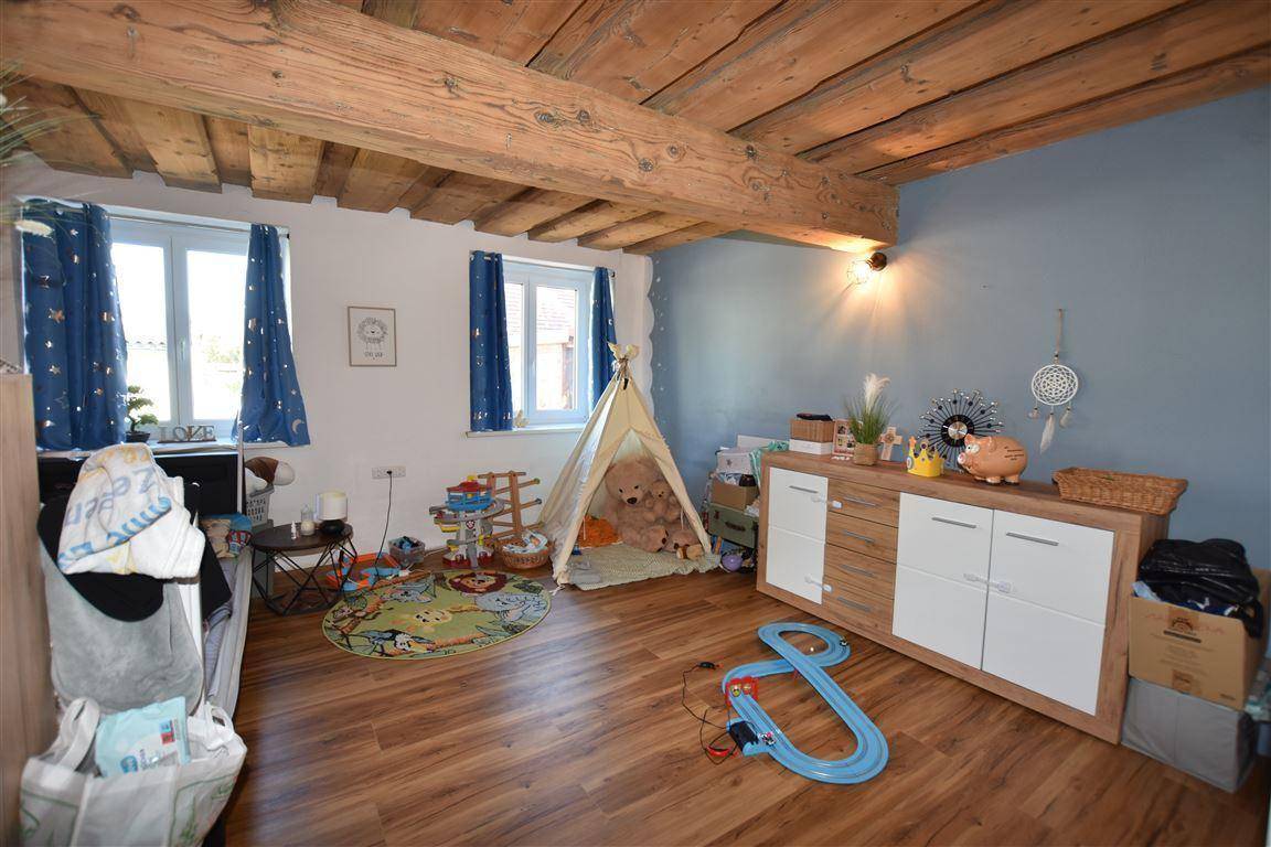 Kinderzimmer mit Holzboden, sichtbaren Deckenbalken und viel natürlichem Licht.