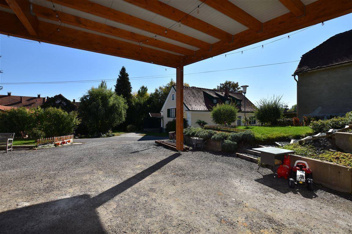 Überdachter Carport und großer Schotterparkplatz vor dem Haus mit Grünflächen.