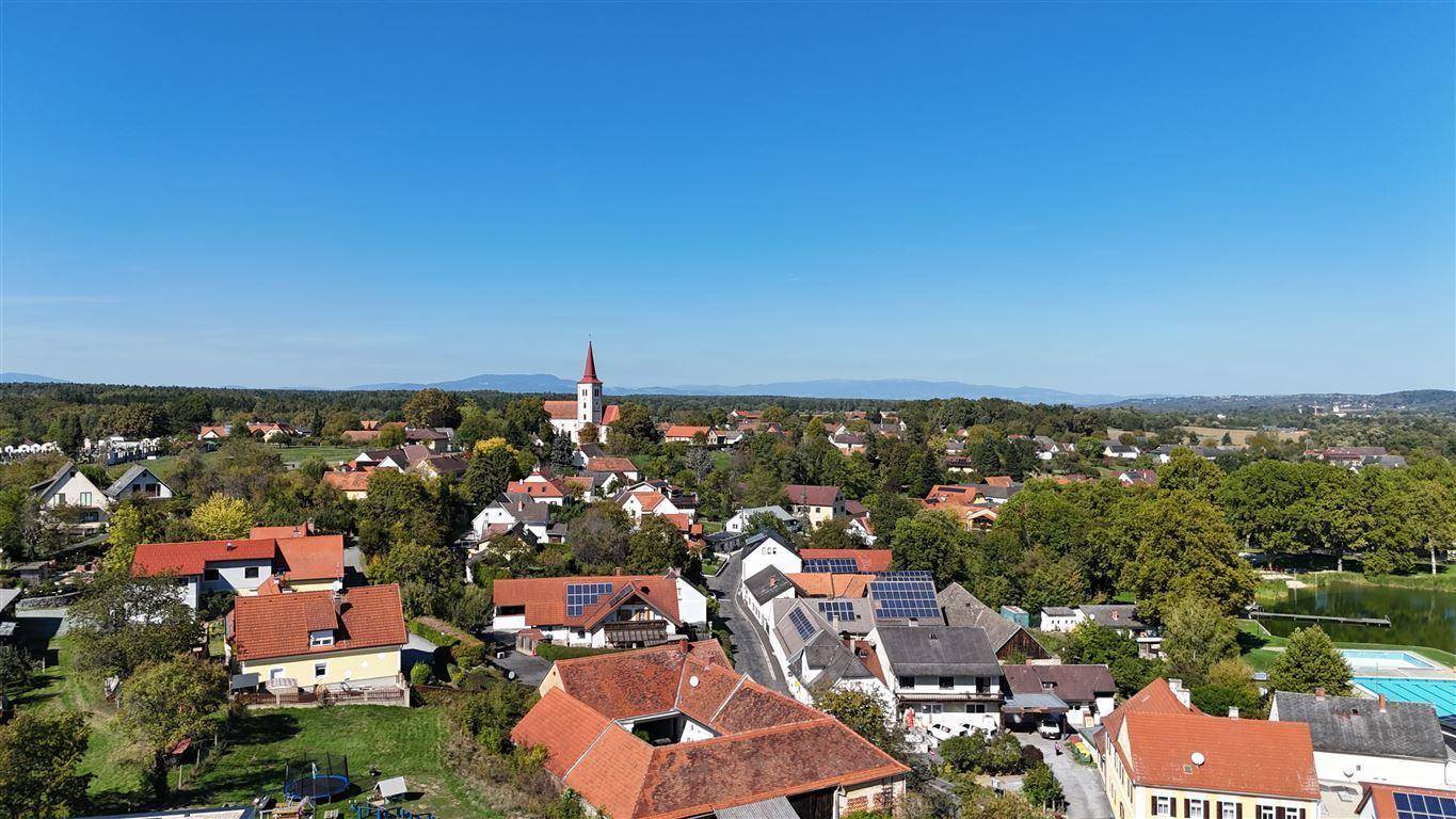 Weitläufige Luftaufnahme einer ländlichen Siedlung mit Häusern, Bäumen und einem See.