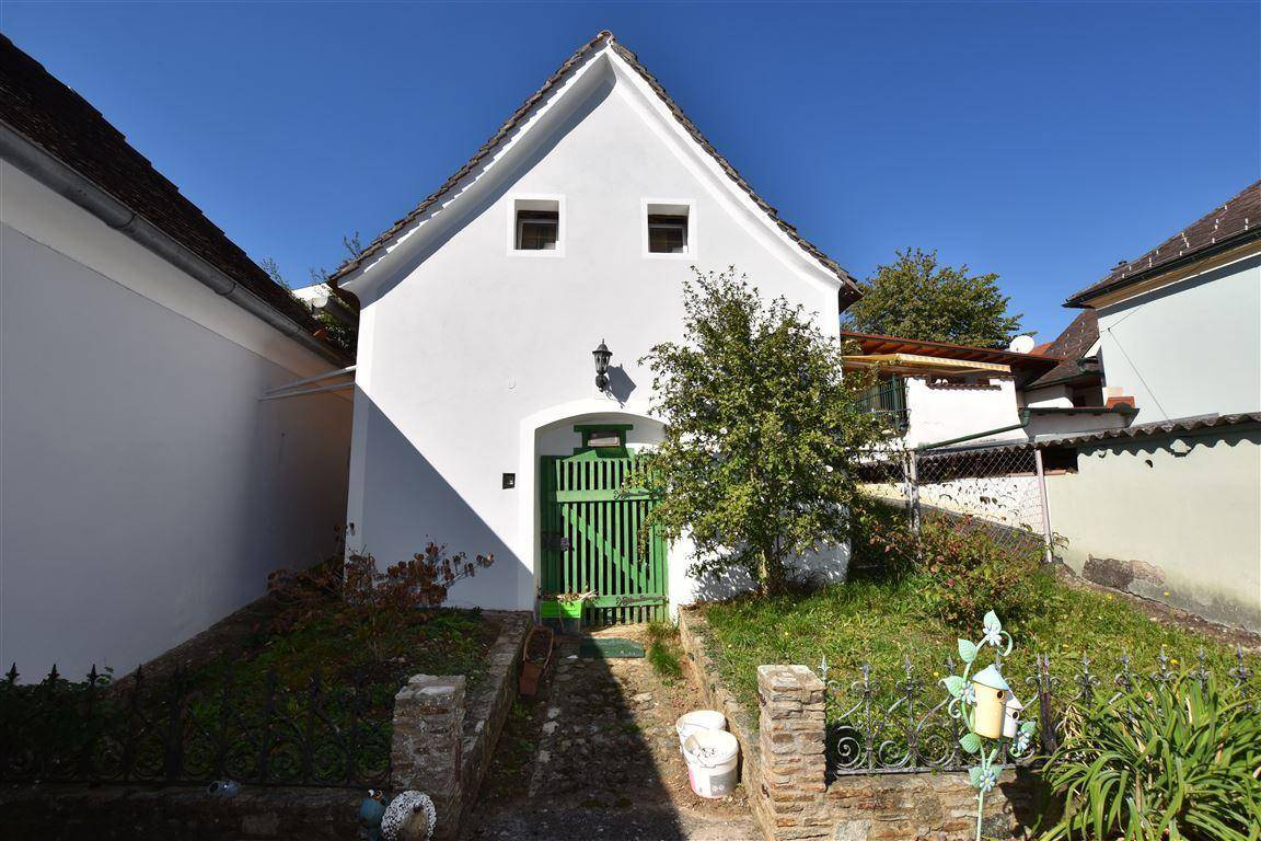 Traditionelles weißes Gebäude mit grünem Tor und Satteldach in ländlicher Umgebung.