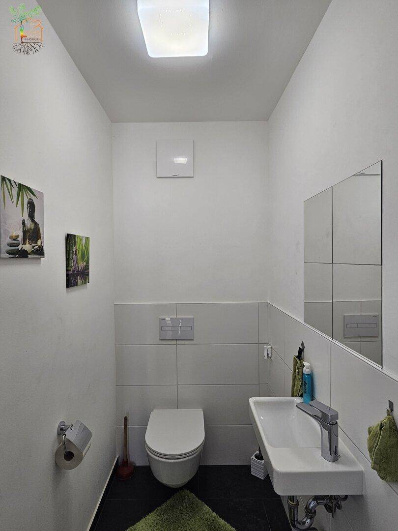 Helles Gäste-WC mit wandhängender Toilette, kleinem Waschbecken und modernen Fliesen.