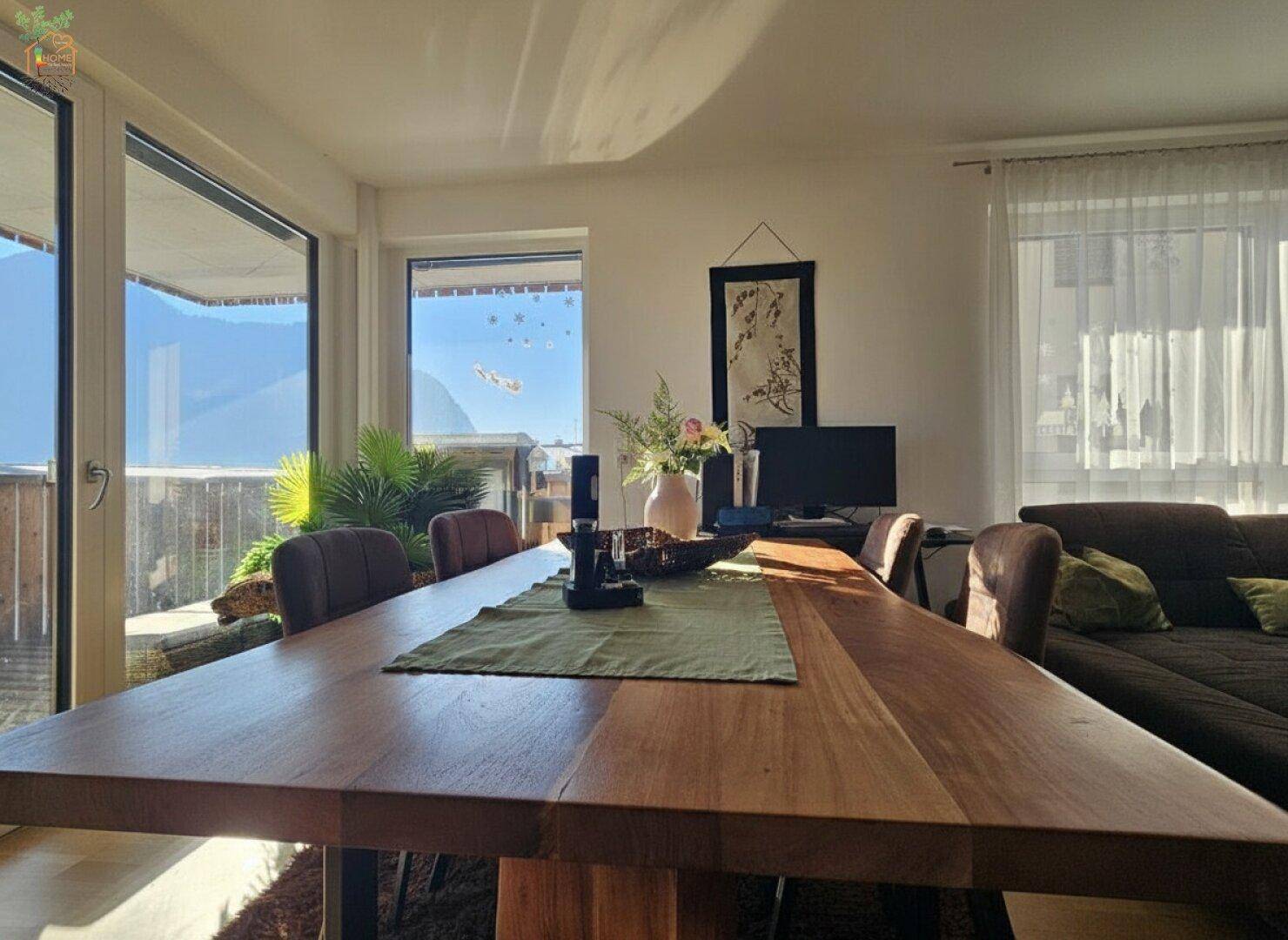Essbereich mit großem Holztisch und direktem Zugang zum Balkon mit Panoramablick auf die Berge.