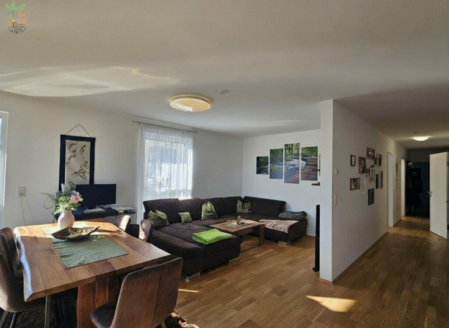 Gemütlicher Wohn- und Essbereich mit bequemer Couch und Holzboden, der in einen Flur übergeht.