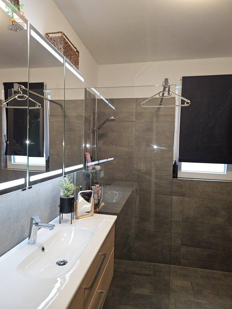 Modernes Badezimmer mit großformatigen Fliesen, ebenerdiger Dusche und Einzelwaschbecken.