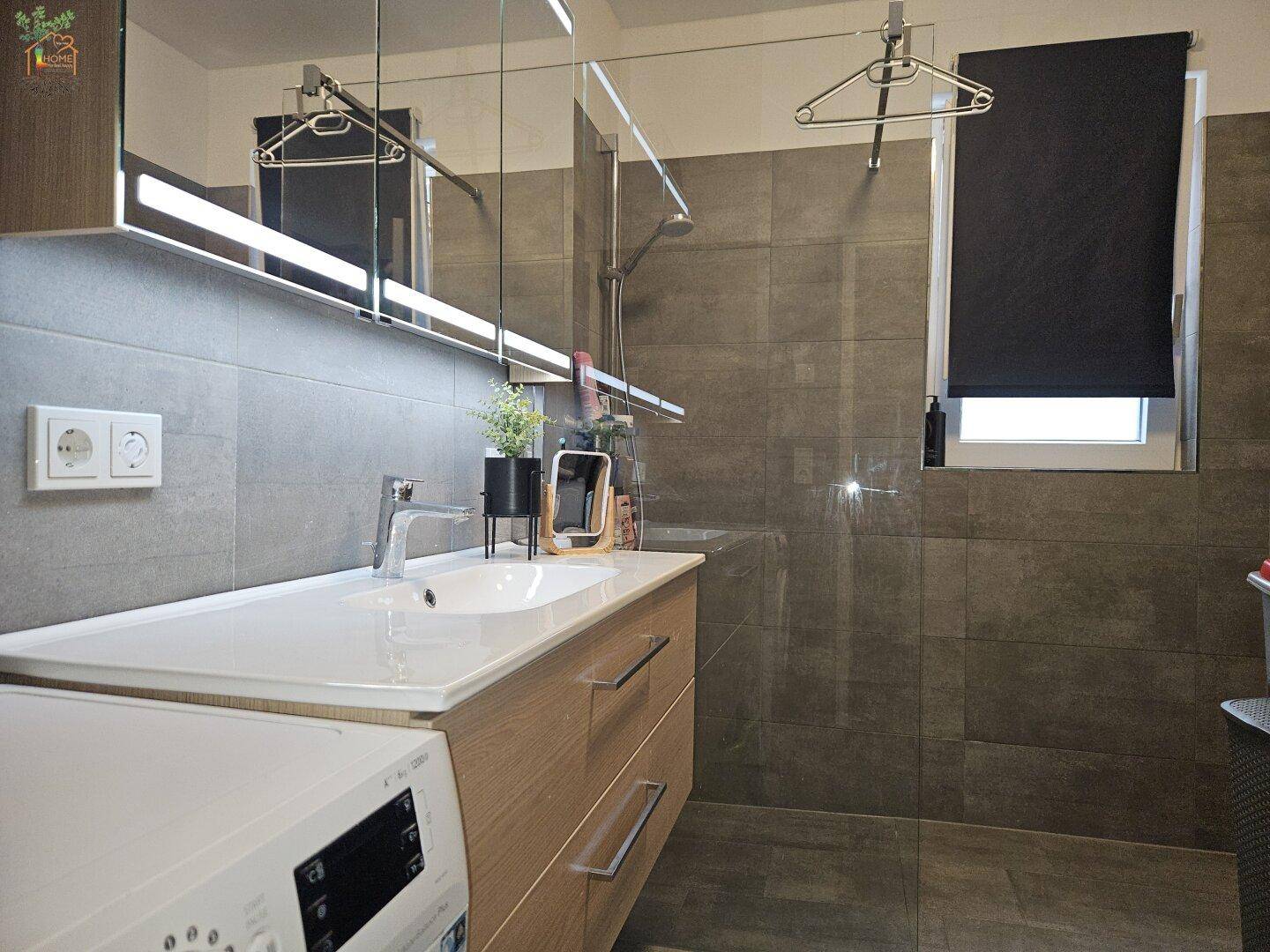 Funktionales Badezimmer mit Dusche, Waschbecken und integrierter Waschmaschine.