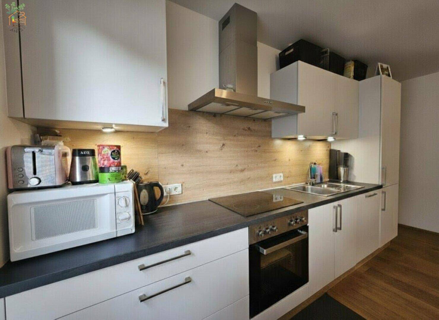 Moderne Einbauküche mit weißen Schränken, dunkler Arbeitsplatte und integrierten Geräten.
