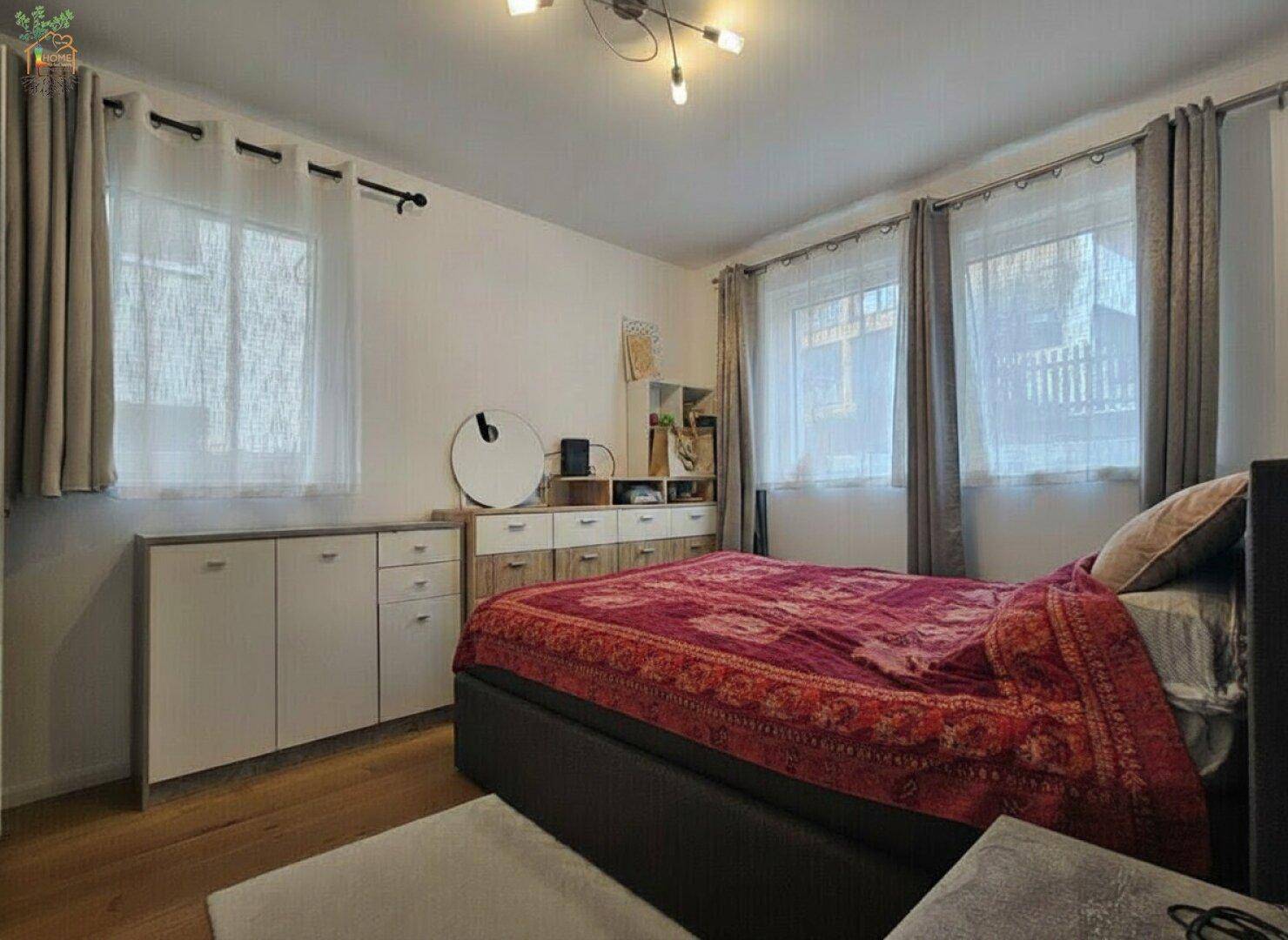 Gemütliches Schlafzimmer mit Holzboden, großem Bett und mehreren Fenstern für viel Licht.