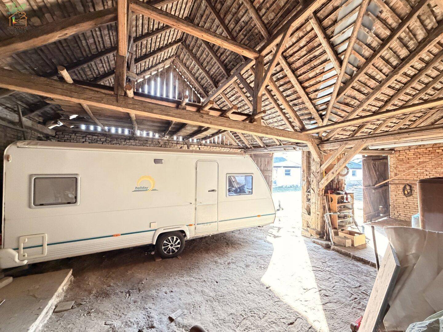 Geräumige Scheune mit sichtbarer Holzkonstruktion und einem geparkten Wohnwagen.