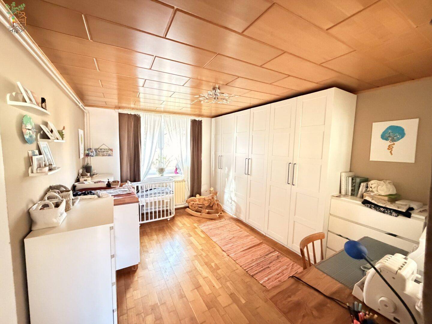 Helles Kinderzimmer mit Babybett, großen weißen Kleiderschränken und Holzfußboden.