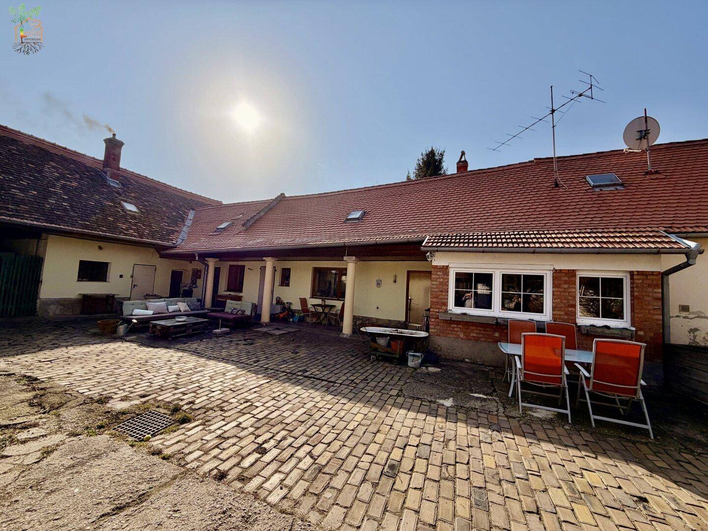 Sonniger Innenhof mit Pflastersteinen, rustikalen Sitzgelegenheiten und Gebäudefassaden.