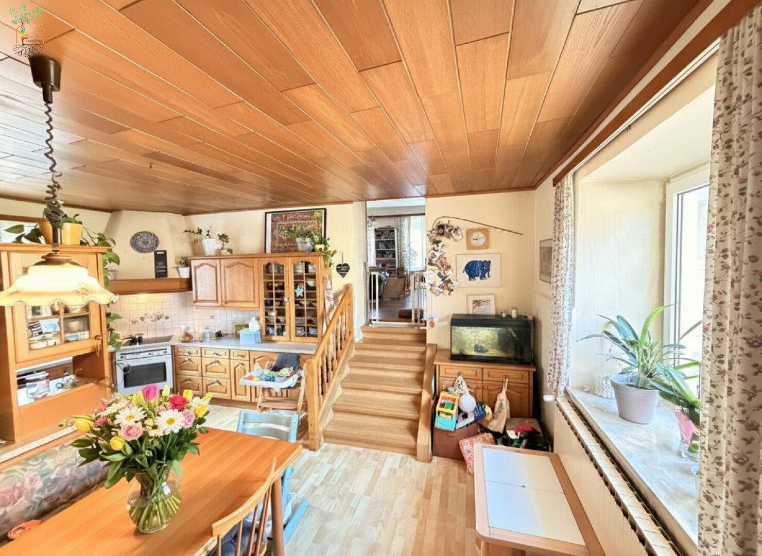 Gemütliche Küche mit Holzeinbauten, Esstisch und Treppe, die zu einem oberen Bereich führt.