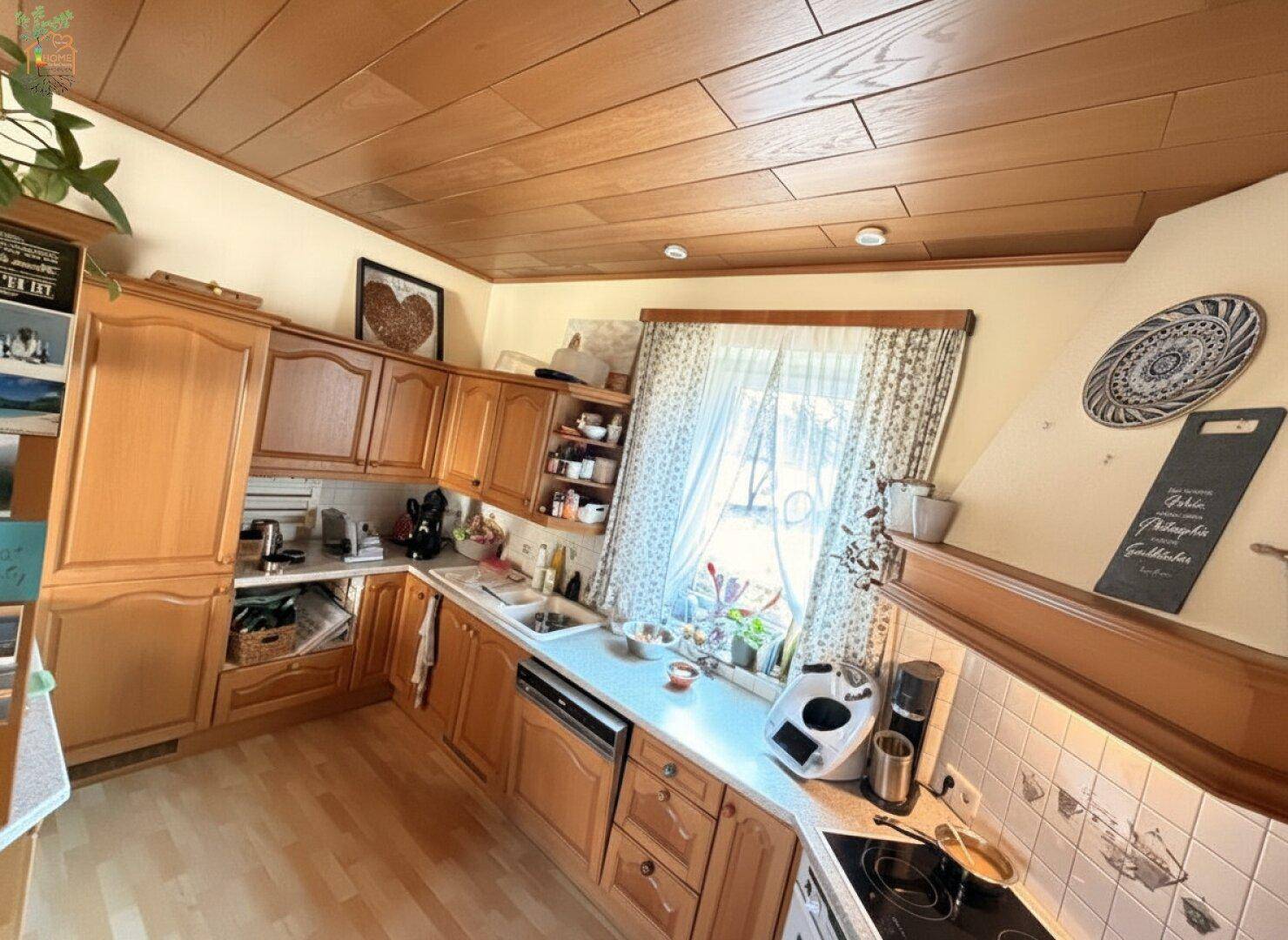 Traditionelle Holzküche mit Einbauschränken, Spüle und Herd, beleuchtet durch ein Fenster.