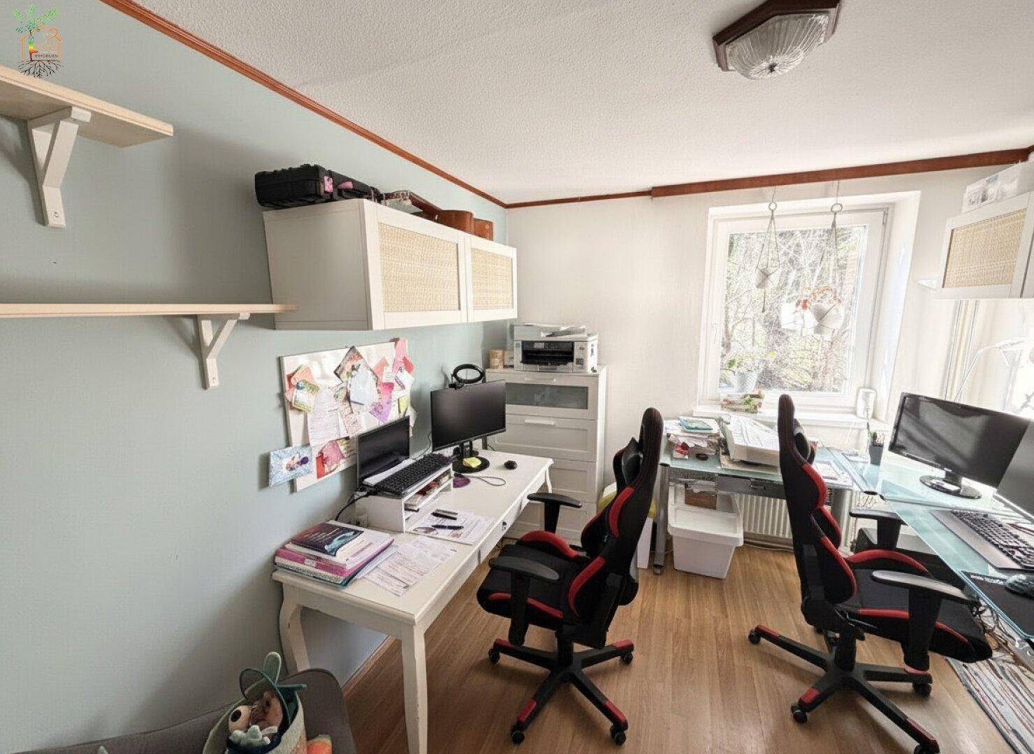 Funktionales Büro mit zwei Schreibtischen, Gaming-Stühlen und natürlichem Lichteinfall.