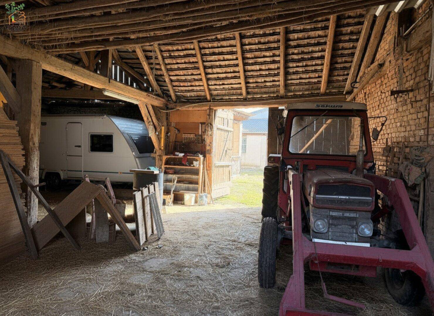 Geräumiger Innenbereich eines Stalls oder einer Scheune mit Traktor und Wohnwagen.