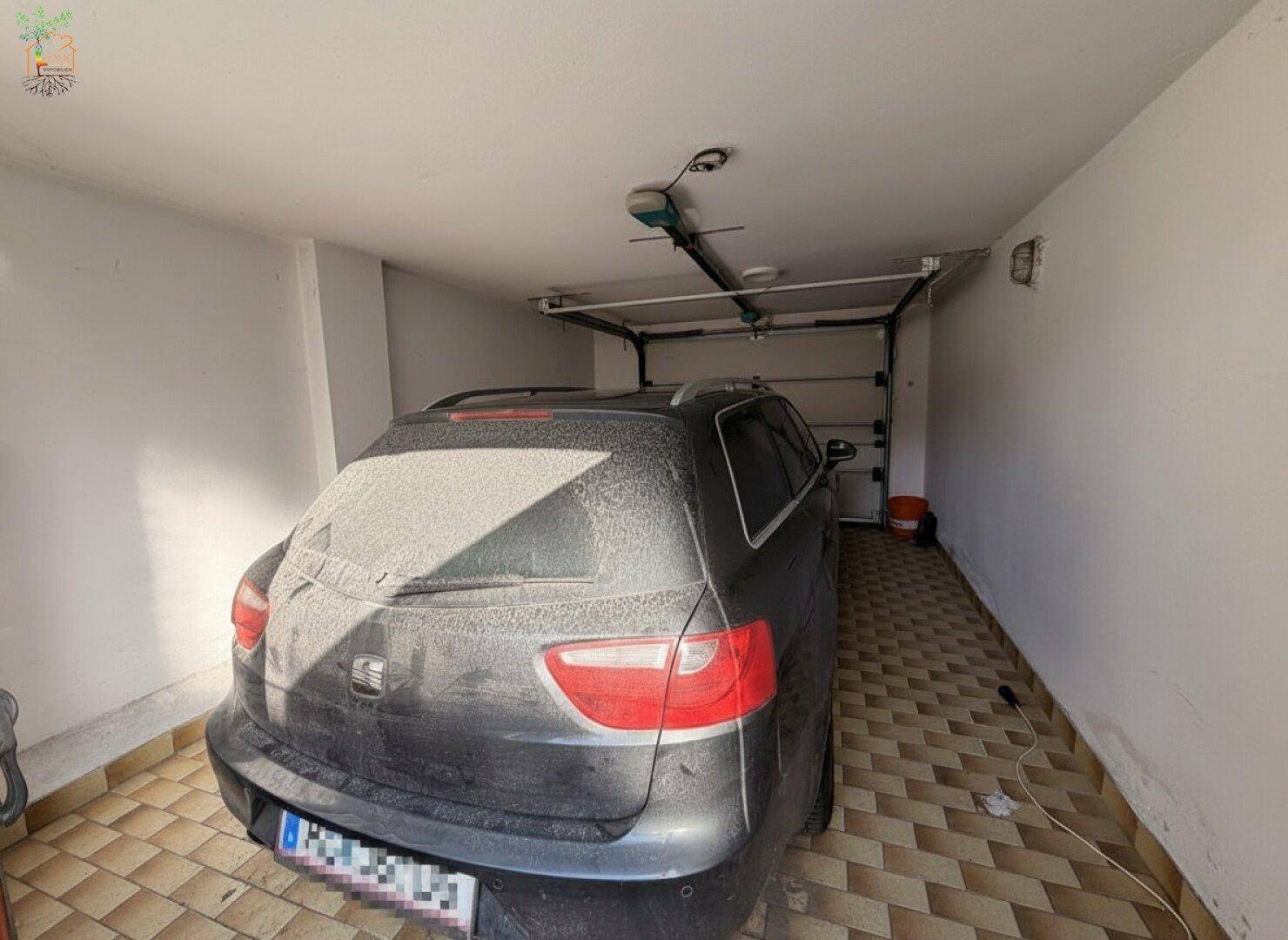 Einzelgarage mit gefliestem Boden, automatischem Tor und einem geparkten, staubigen Auto.
