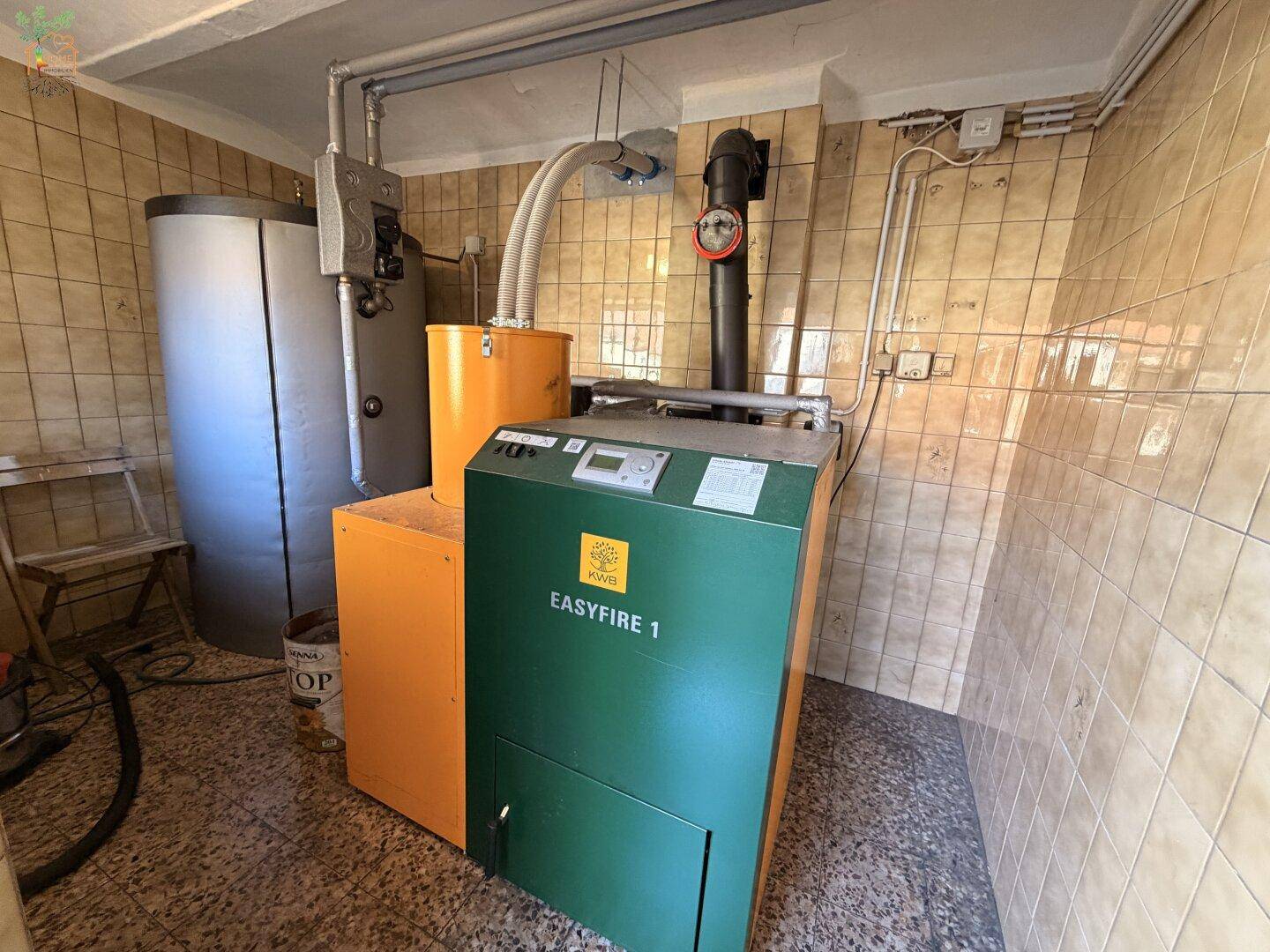 Heizungsraum mit Pelletkessel und Warmwasserspeicher, gefliesten Wänden und Boden.