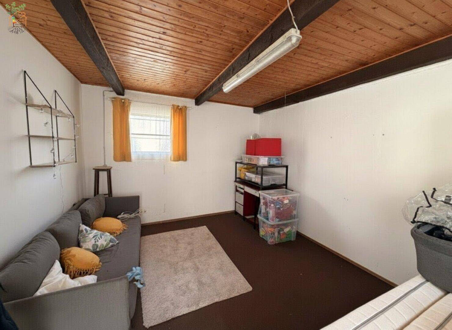Raum mit Sofa, Holzdecke und sichtbaren Balken, bietet vielseitige Nutzungsmöglichkeiten.