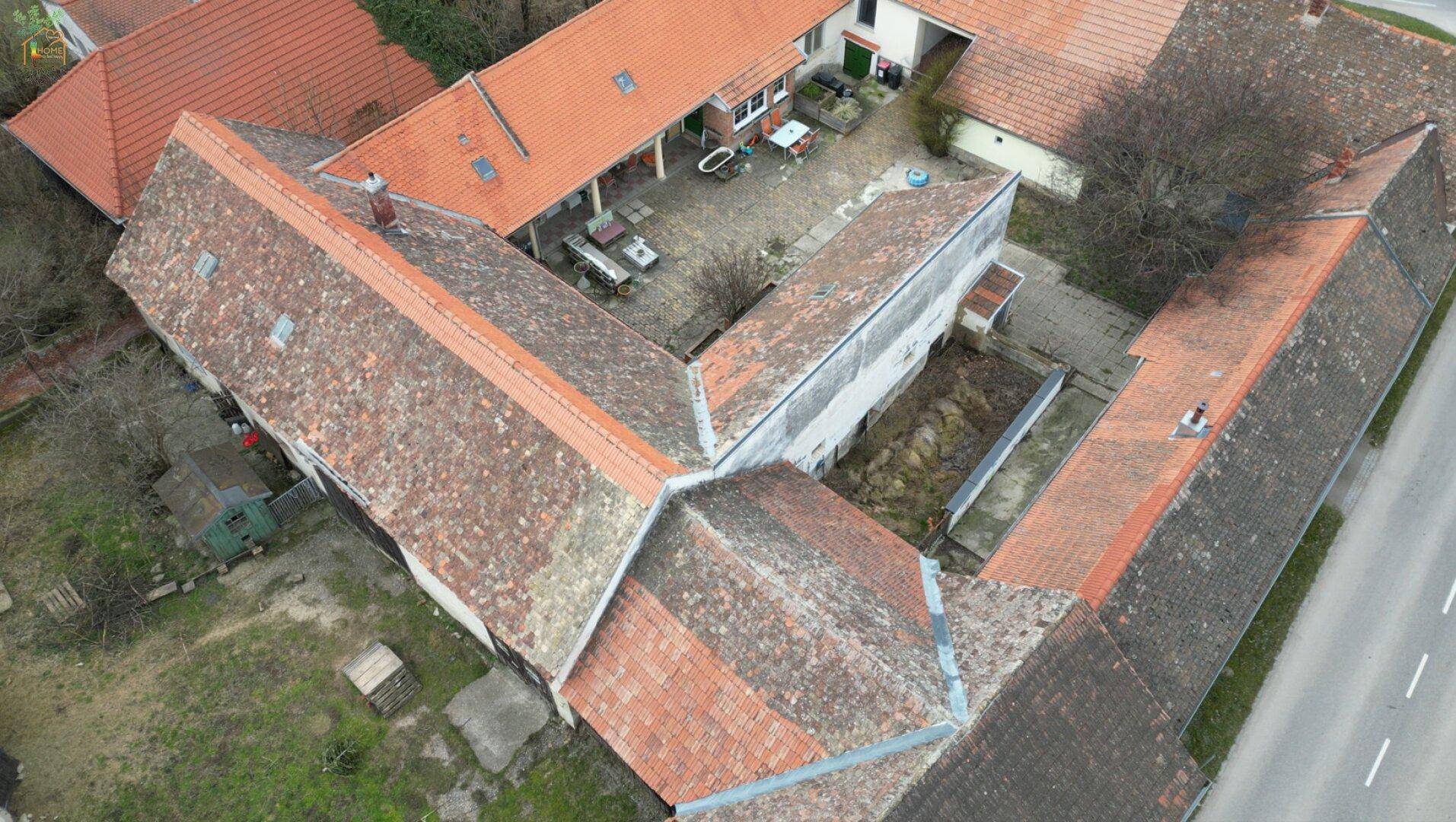 Luftaufnahme eines weitläufigen Anwesens mit mehreren Gebäuden und roten Ziegeldächern.