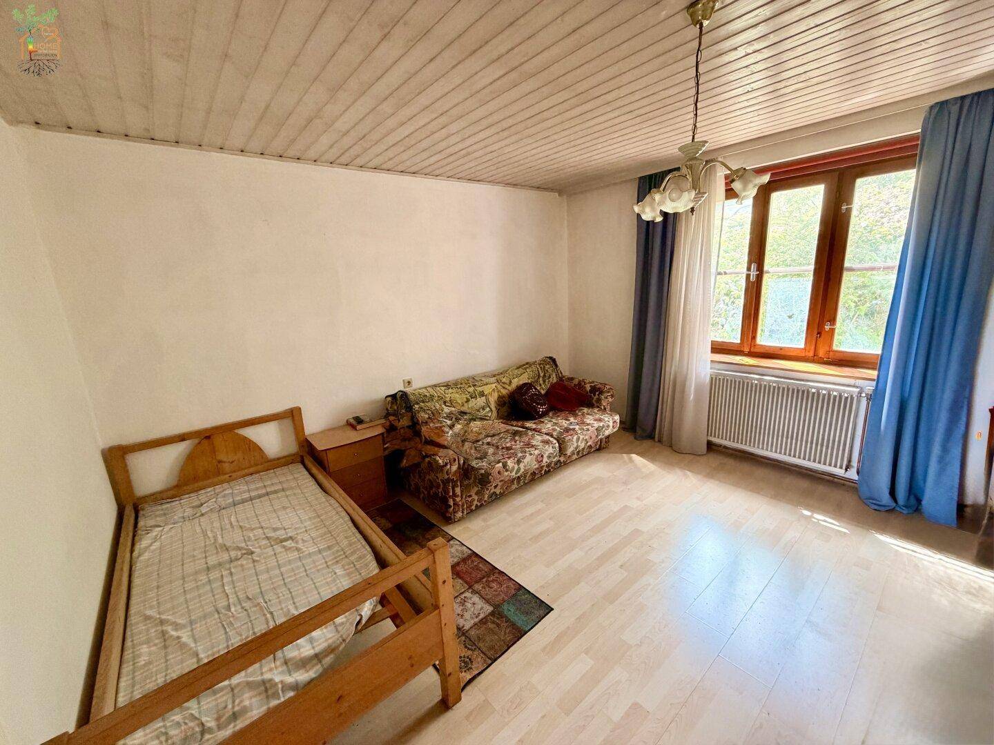Helles Zimmer mit Holzdecken, Parkettboden und einem Sofa, ideal als Wohn- oder Gästezimmer.