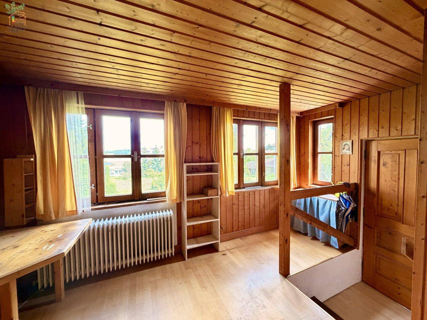 Rustikaler Wohnbereich mit Holzvertäfelung, Holzboden und weitem Blick in die Landschaft.