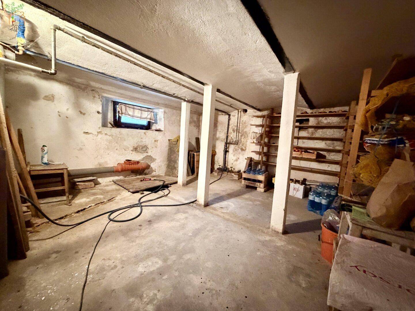 Unausgebauter Kellerraum mit Betonboden, sichtbaren Rohren und kleinem Fenster.