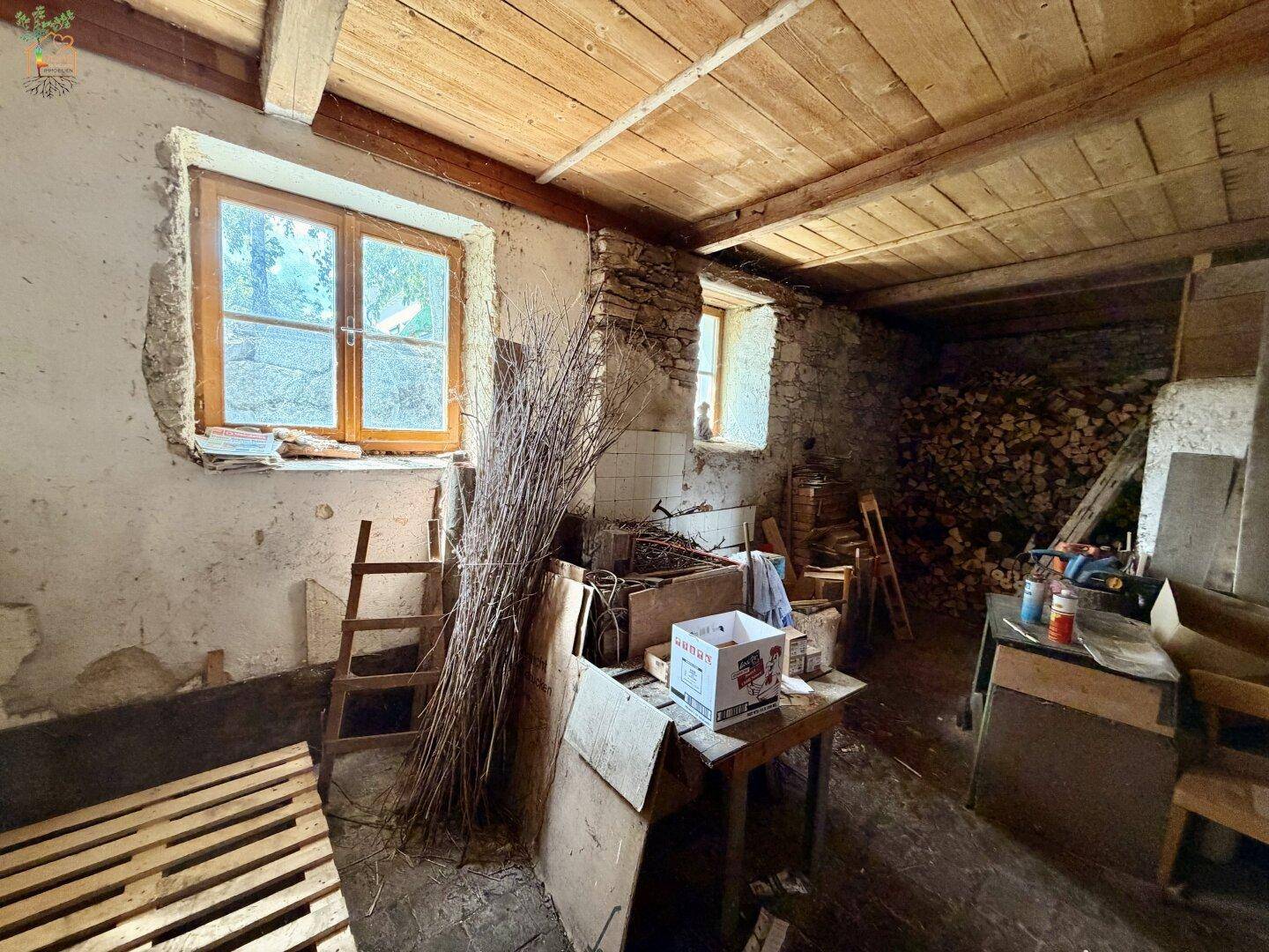 Rustikaler Lagerraum mit Steinwänden, Holzbalken und Holzvorräten.
