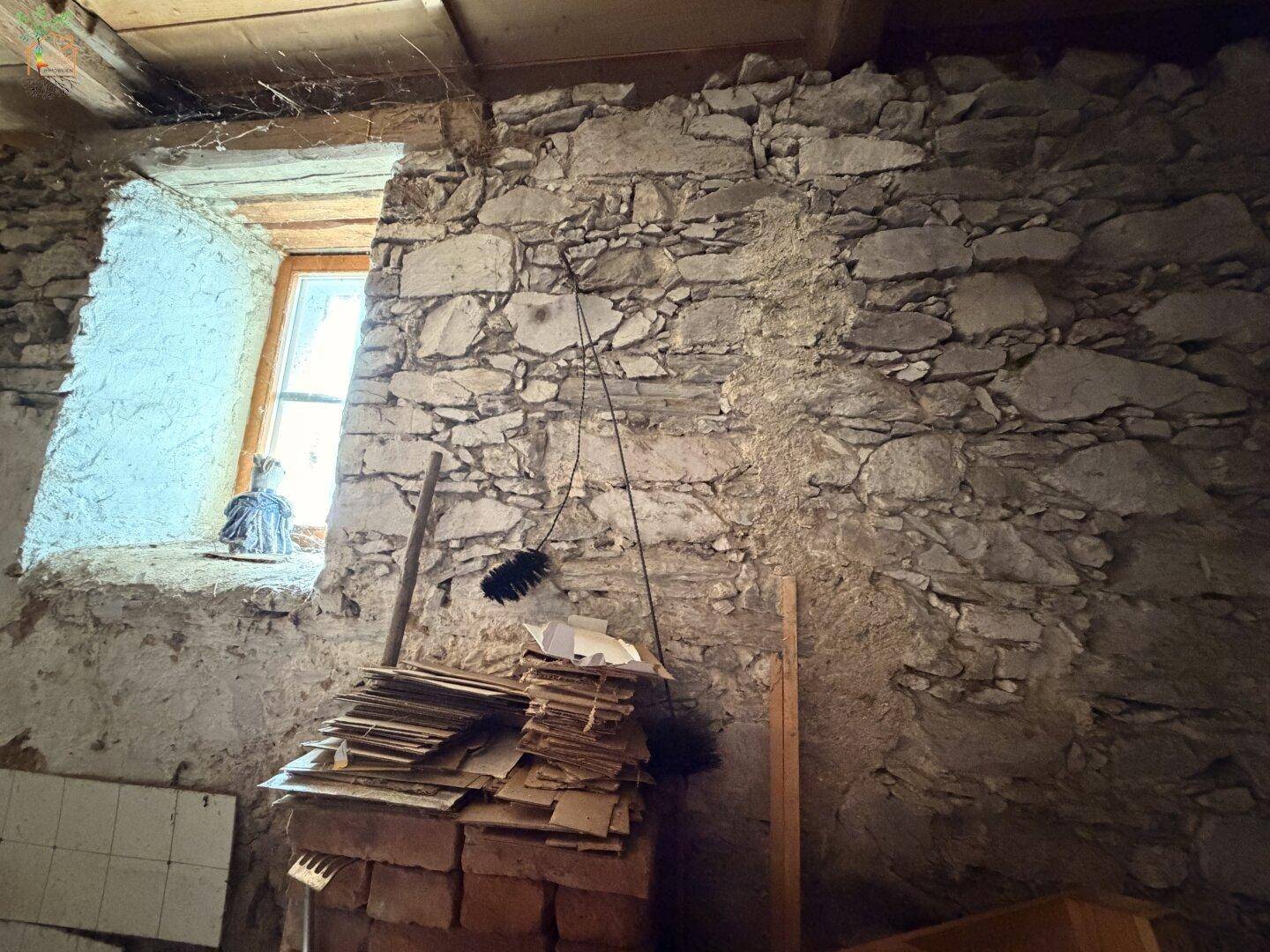 Alter Lagerraum mit groben Steinwänden und kleinem Fenster, in ursprünglichem Zustand.