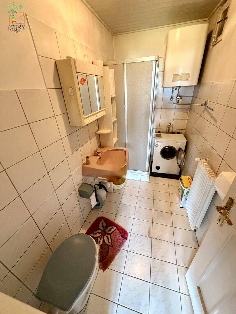 Kleines Badezimmer mit Dusche, WC, Waschbecken und Fliesen an Wänden und Boden.