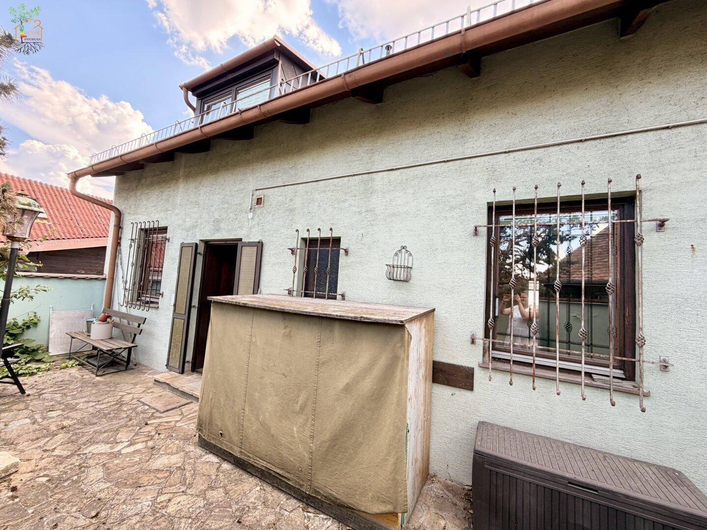 Kleine gepflasterte Terrasse an der Hauswand mit Sitzbank und Blick in den Garten.