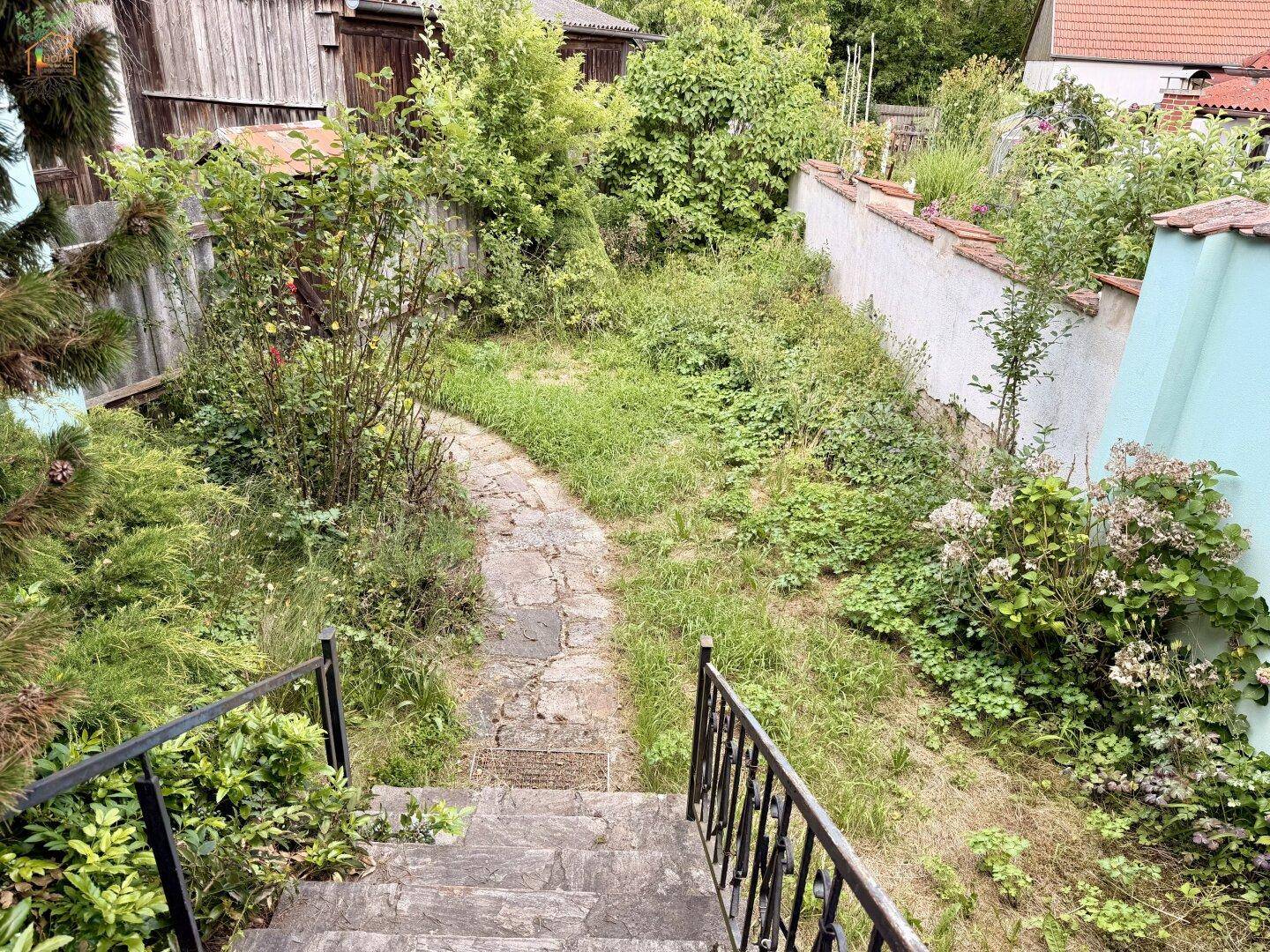 Treppe führt hinunter in einen verwilderten Gartenbereich mit Steinpfad.
