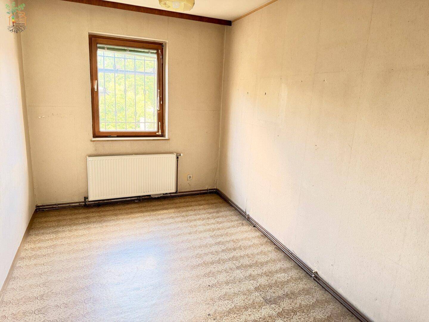 Kleines Schlafzimmer mit gemustertem Bodenbelag, Holzdecke und einem Fenster.