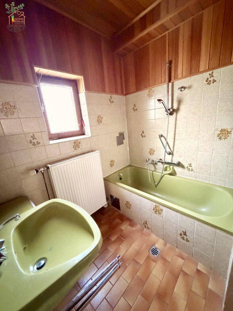 Badezimmer im 80er-Jahre-Stil mit grüner Badewanne, Waschbecken und gemusterten Fliesen.