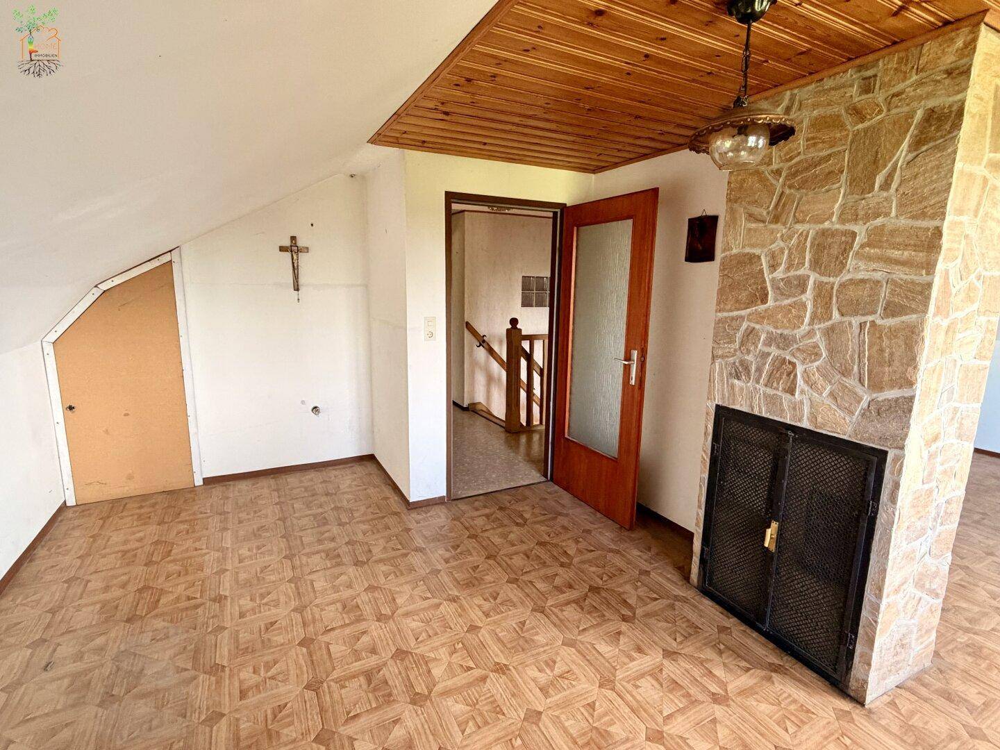 Dachgeschossraum mit Holzbalken, Steinwand und gemustertem Bodenbelag.