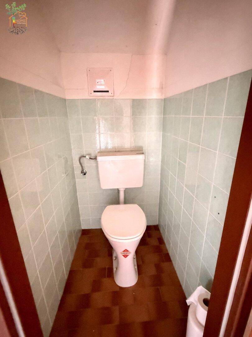 Kleine Toilette mit hellgrünen Fliesen und Terrakotta-Bodenfliesen.