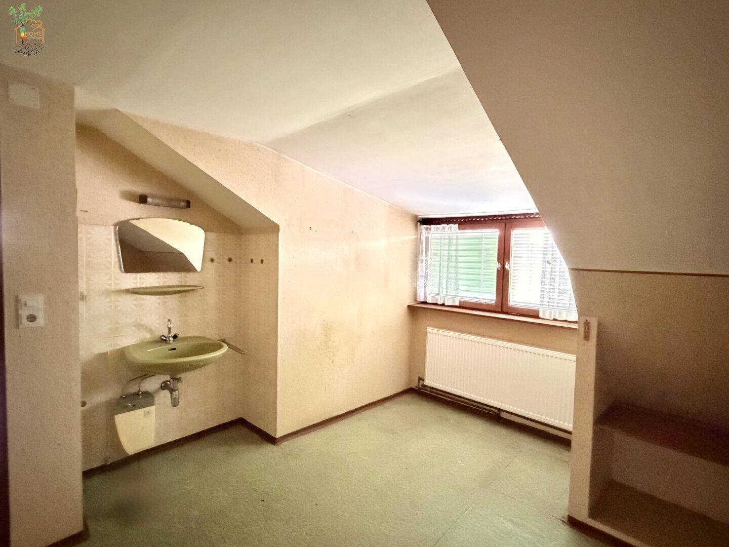 Dachgeschossraum mit Waschbecken, schrägen Wänden und Fenster.
