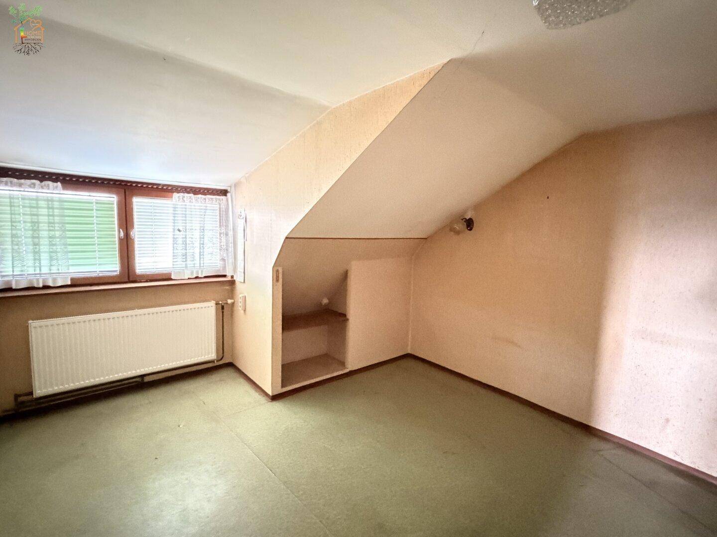 Dachgeschossraum mit schrägen Wänden, Fenster und integrierten Regalen.